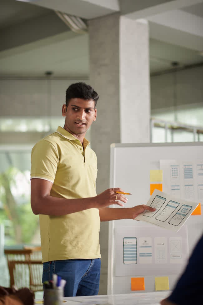 UX Designer Speaking in Meeting Image of an Indian UX designer presenting a storyboard representing the concept of learning experience design.